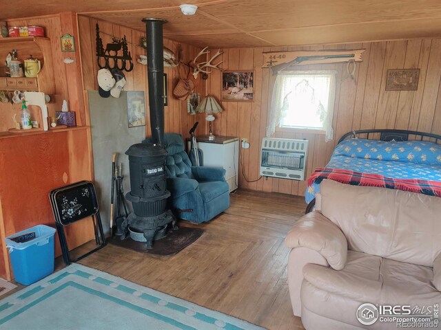 bedroom featuring a wood stove, wooden walls, wood-type flooring, wood ceiling, and heating unit