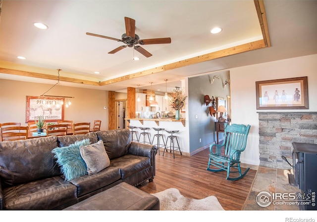 living room with a raised ceiling, a wood stove, ceiling fan, and hardwood / wood-style floors