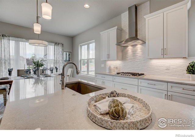 kitchen featuring pendant lighting, white cabinetry, sink, stainless steel gas cooktop, and wall chimney exhaust hood