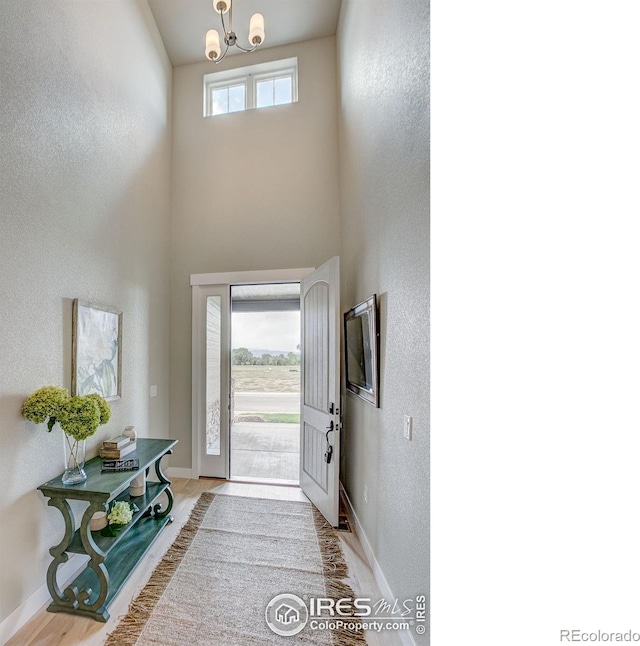 foyer featuring a high ceiling, light wood-type flooring, a wealth of natural light, and a chandelier