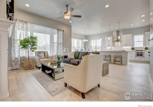 living room featuring sink, light hardwood / wood-style flooring, and ceiling fan