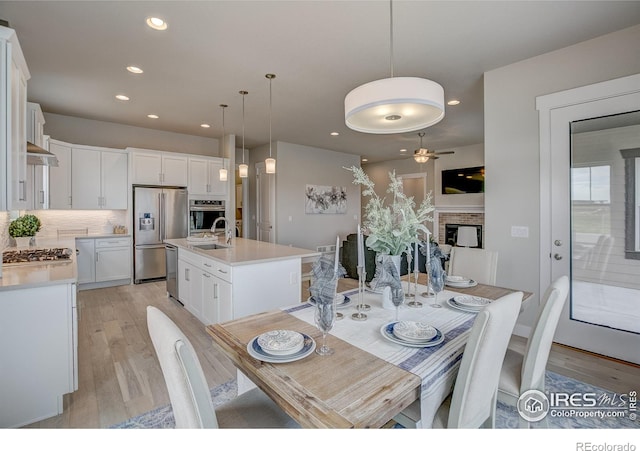 dining space with sink, a fireplace, ceiling fan, and light wood-type flooring