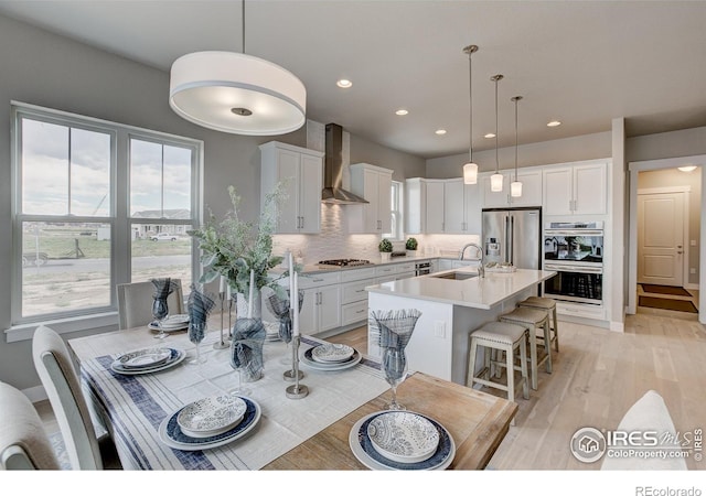 kitchen with white cabinetry, appliances with stainless steel finishes, wall chimney exhaust hood, and an island with sink