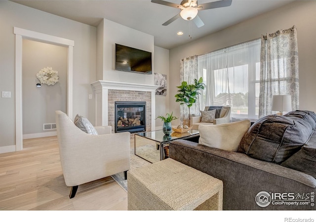 living room featuring a fireplace, light hardwood / wood-style floors, and ceiling fan