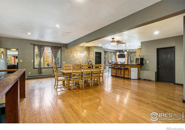 dining space featuring light wood-type flooring, beamed ceiling, a baseboard heating unit, and ceiling fan with notable chandelier