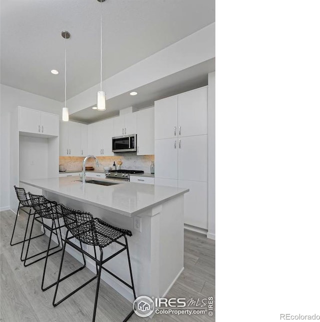 kitchen with light wood-type flooring, a breakfast bar, backsplash, stainless steel appliances, and white cabinets