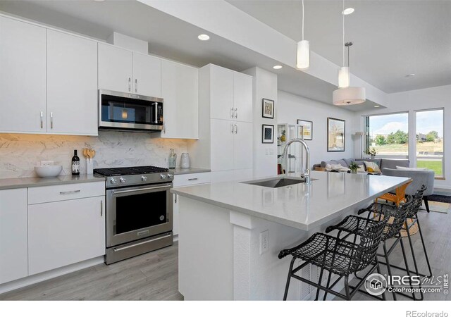 kitchen featuring decorative light fixtures, appliances with stainless steel finishes, light hardwood / wood-style floors, sink, and an island with sink