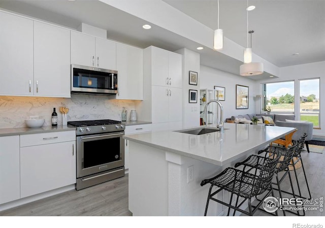 kitchen featuring pendant lighting, light wood-style flooring, a sink, stainless steel appliances, and decorative backsplash