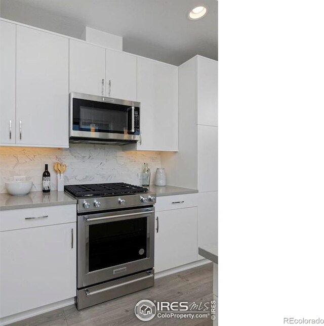 kitchen with appliances with stainless steel finishes, decorative backsplash, white cabinetry, and light hardwood / wood-style flooring