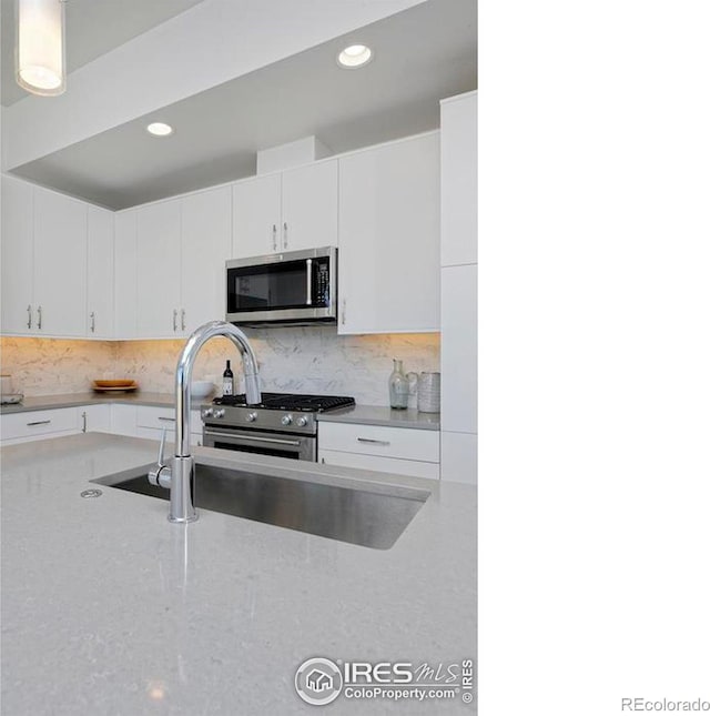 kitchen with tasteful backsplash, appliances with stainless steel finishes, white cabinetry, and light stone counters