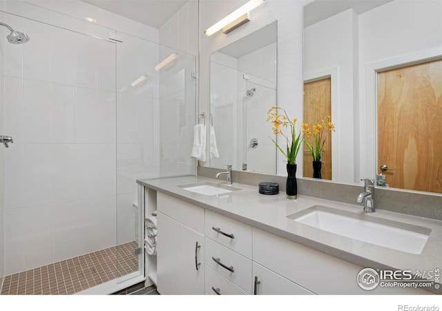 full bath featuring a tile shower, double vanity, and a sink