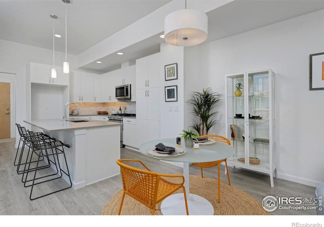 kitchen with light wood-type flooring, pendant lighting, stainless steel appliances, and white cabinets