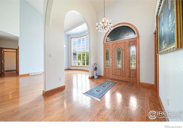 foyer entrance with an inviting chandelier, high vaulted ceiling, and light wood-type flooring