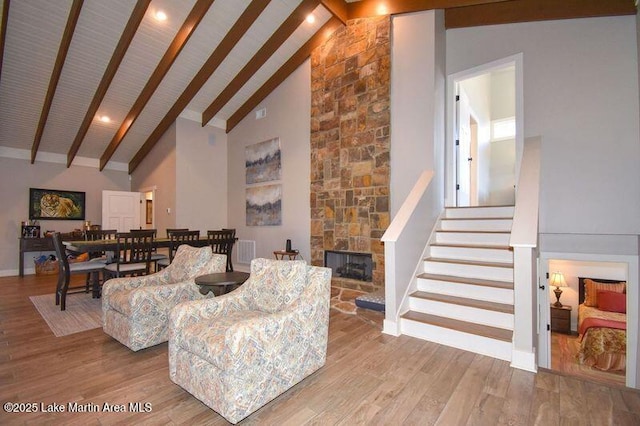 living room with wood finished floors, high vaulted ceiling, a fireplace, stairs, and beamed ceiling