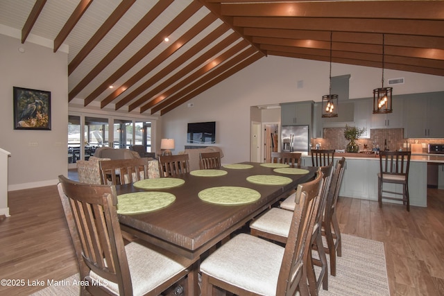 dining space featuring light wood finished floors, visible vents, baseboards, beam ceiling, and high vaulted ceiling