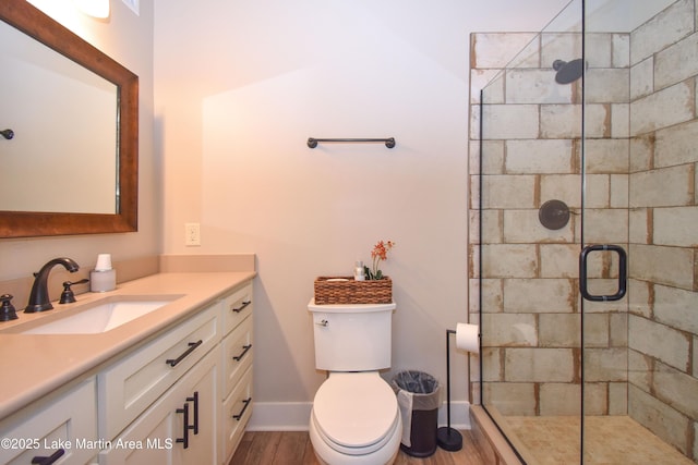 full bathroom with a shower stall, baseboards, toilet, wood finished floors, and vanity