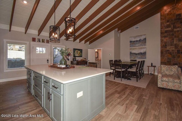 kitchen with wood finished floors, a kitchen island, beam ceiling, light countertops, and pendant lighting