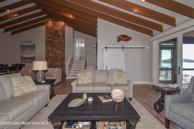 living area featuring stairway, vaulted ceiling with beams, a barn door, and wood finished floors