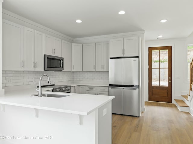 kitchen with stainless steel appliances, a peninsula, a sink, light countertops, and a kitchen bar