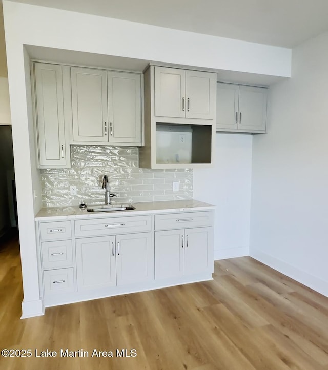 kitchen featuring tasteful backsplash, light wood-style flooring, gray cabinetry, a sink, and baseboards