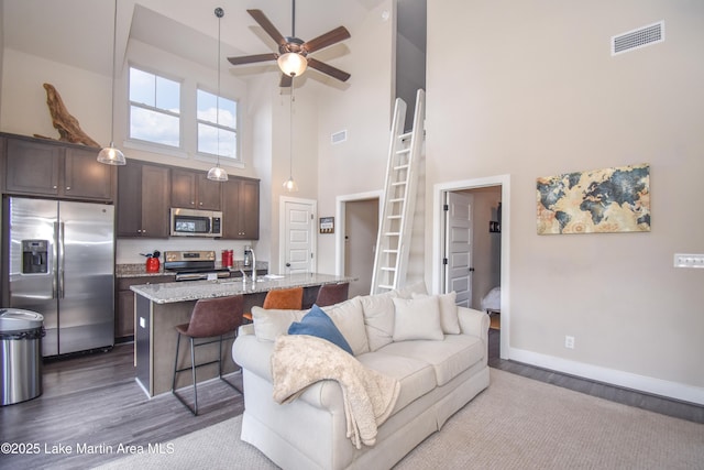 living room with ceiling fan, sink, wood-type flooring, and a high ceiling