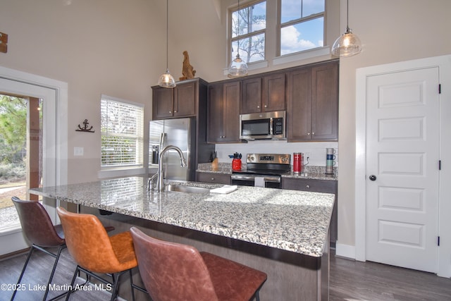 kitchen with light stone countertops, sink, hanging light fixtures, dark brown cabinets, and appliances with stainless steel finishes