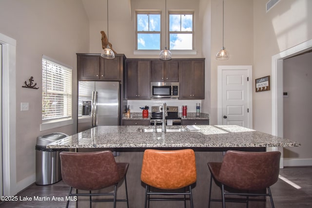 kitchen with a high ceiling, sink, light stone countertops, dark brown cabinets, and stainless steel appliances