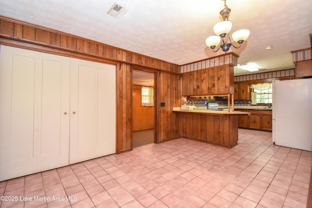 300 Hornsby Dr, Tallassee, AL 36078 - kitchen with freestanding refrigerator, a peninsula, wooden walls, brown cabinetry, and a chandelier