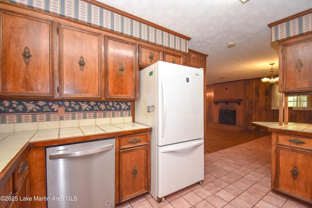 300 Hornsby Dr, Tallassee, AL 36078 - kitchen with freestanding refrigerator, stainless steel dishwasher, tile counters, brown cabinets, and a textured ceiling