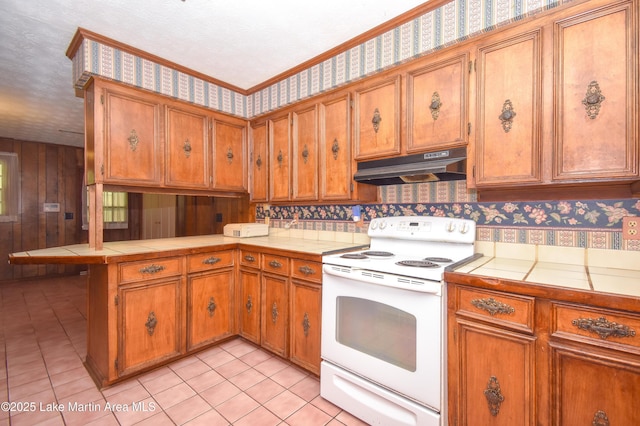 300 Hornsby Dr, Tallassee, AL 36078 - kitchen featuring white electric stove, under cabinet range hood, tile countertops, brown cabinets, and wallpapered walls