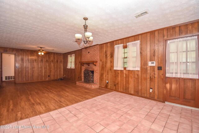 300 Hornsby Dr, Tallassee, AL 36078 - unfurnished living room with a chandelier, ceiling fan, wood finished floors, wood walls, and a fireplace