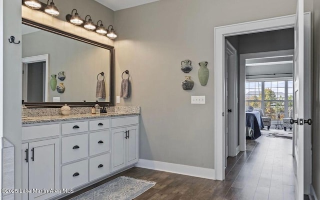 ensuite bathroom with double vanity, wood finished floors, baseboards, ensuite bathroom, and a sink
