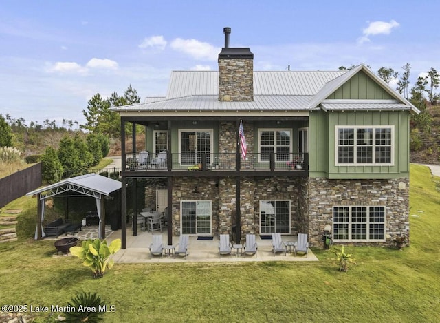 rear view of property featuring board and batten siding, a yard, a balcony, and stone siding