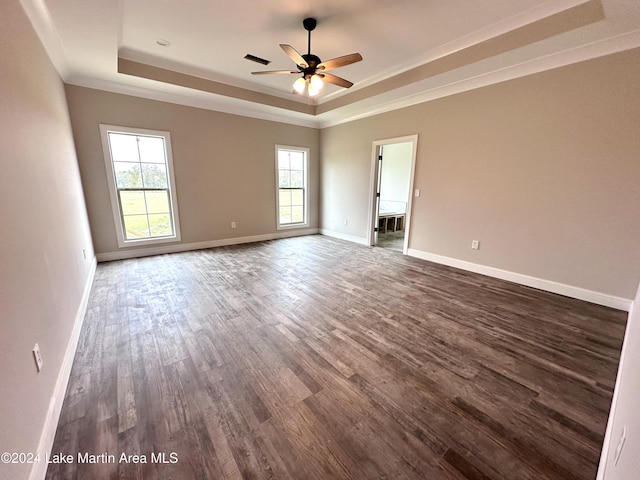 empty room featuring ceiling fan, a tray ceiling, a wealth of natural light, and dark hardwood / wood-style floors