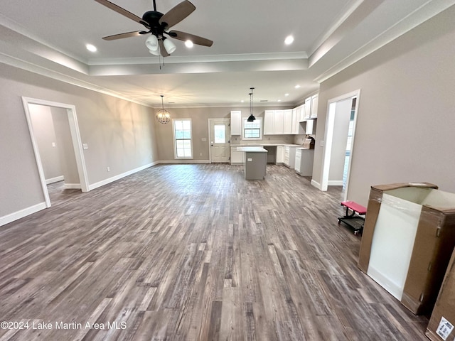 unfurnished living room with a raised ceiling, crown molding, hardwood / wood-style floors, and ceiling fan with notable chandelier