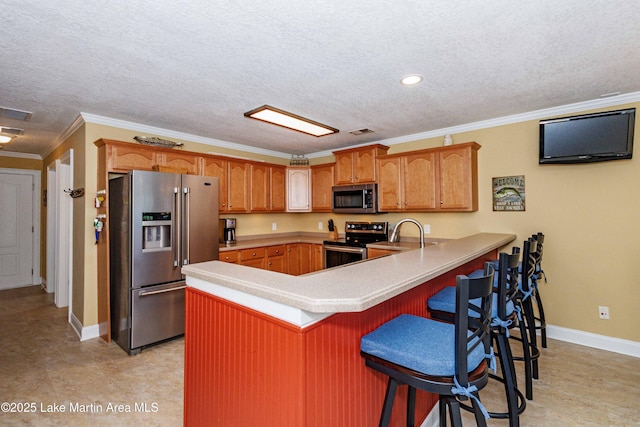 kitchen with stainless steel appliances, a peninsula, a textured ceiling, baseboards, and a kitchen bar