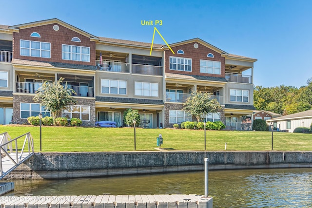 rear view of house featuring a yard, a ceiling fan, a water view, and a balcony