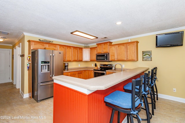 kitchen with a breakfast bar, ornamental molding, a textured ceiling, kitchen peninsula, and stainless steel appliances