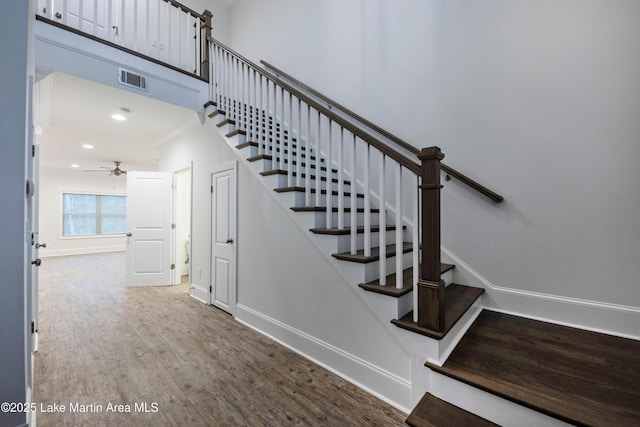 stairway with a high ceiling, wood-type flooring, ceiling fan, and crown molding