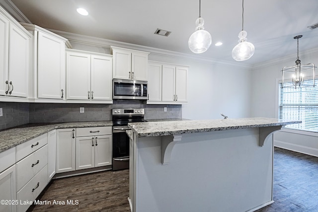 kitchen featuring appliances with stainless steel finishes, hanging light fixtures, a kitchen breakfast bar, white cabinets, and a center island with sink