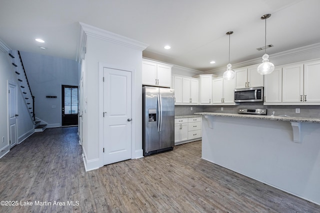 kitchen with light stone counters, hardwood / wood-style flooring, pendant lighting, stainless steel appliances, and white cabinets