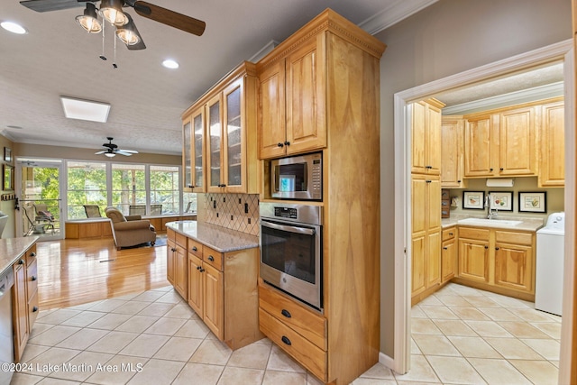 kitchen featuring appliances with stainless steel finishes, crown molding, sink, light tile patterned floors, and washer / dryer