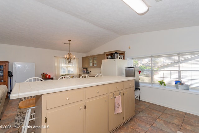 100 Royal Dr, Equality, AL 36026 - kitchen with an inviting chandelier, freestanding refrigerator, vaulted ceiling, tile counters, and pendant lighting