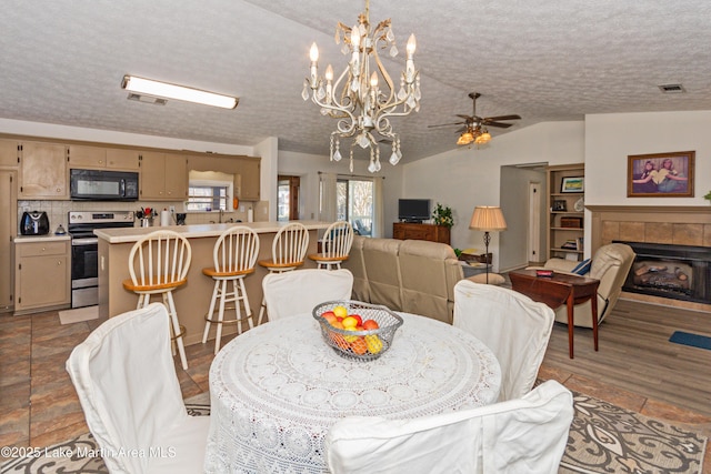 100 Royal Dr, Equality, AL 36026 - dining room featuring visible vents, lofted ceiling, a tile fireplace, a textured ceiling, and ceiling fan with notable chandelier