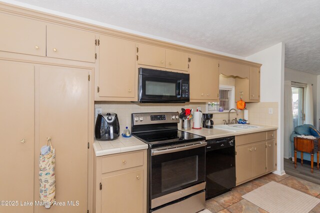 100 Royal Dr, Equality, AL 36026 - kitchen with cream cabinetry, black appliances, a sink, tile countertops, and decorative backsplash