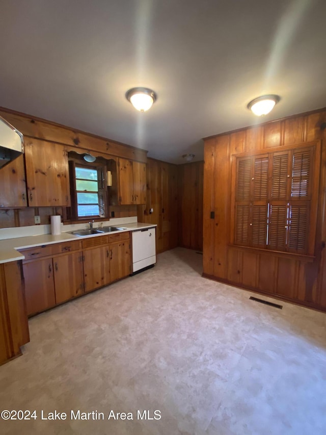 kitchen featuring white dishwasher, sink, and wooden walls