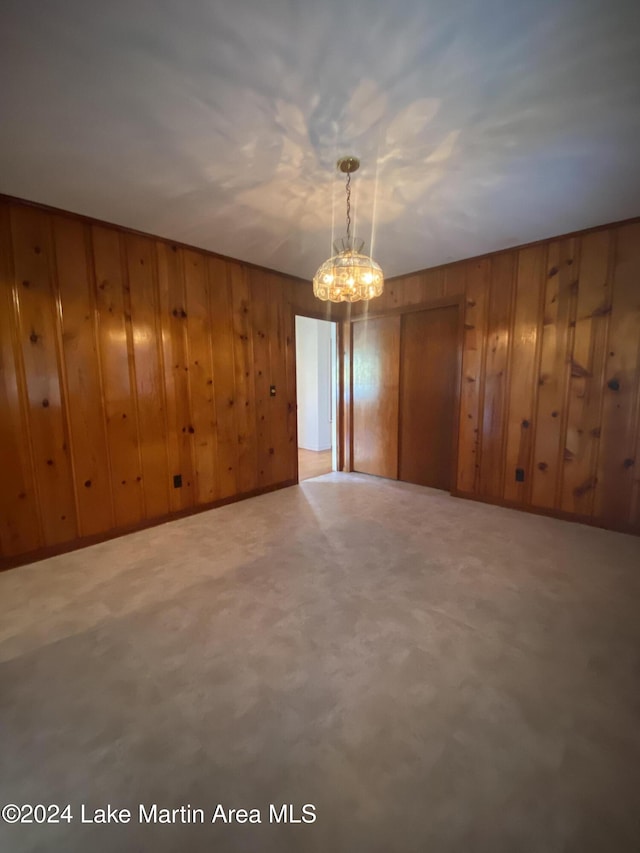 unfurnished room with an inviting chandelier and wooden walls