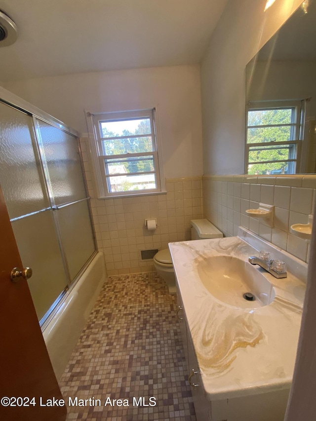 full bathroom featuring plenty of natural light, toilet, shower / bath combination with glass door, and tile walls