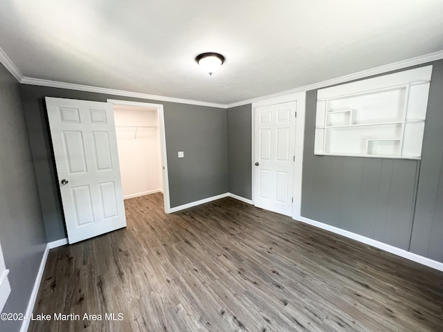 unfurnished bedroom featuring a spacious closet, a closet, ornamental molding, and hardwood / wood-style flooring