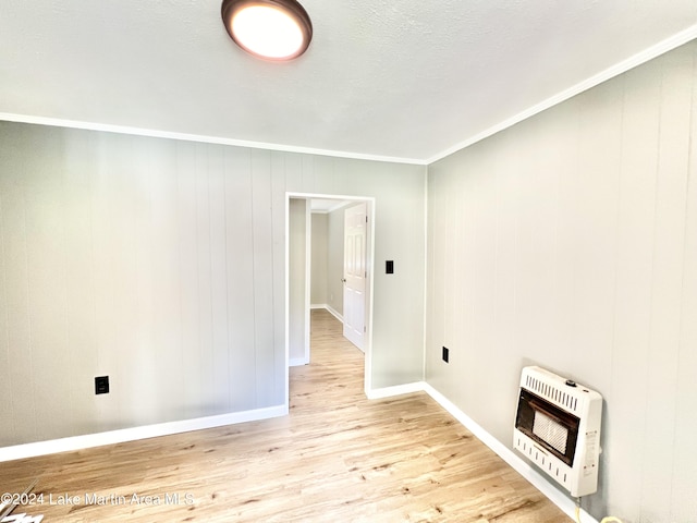 empty room with heating unit, crown molding, light hardwood / wood-style flooring, and wooden walls